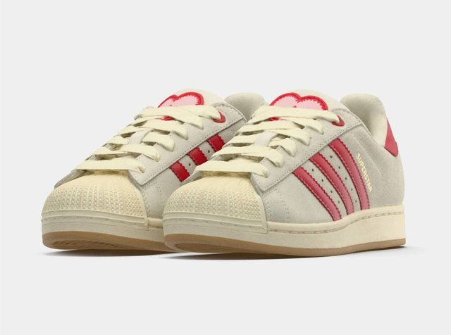 Zapatillas Adidas color crema con rayas rosas, punteras texturizadas y suelas de goma, mostradas lado a lado sobre un fondo blanco.