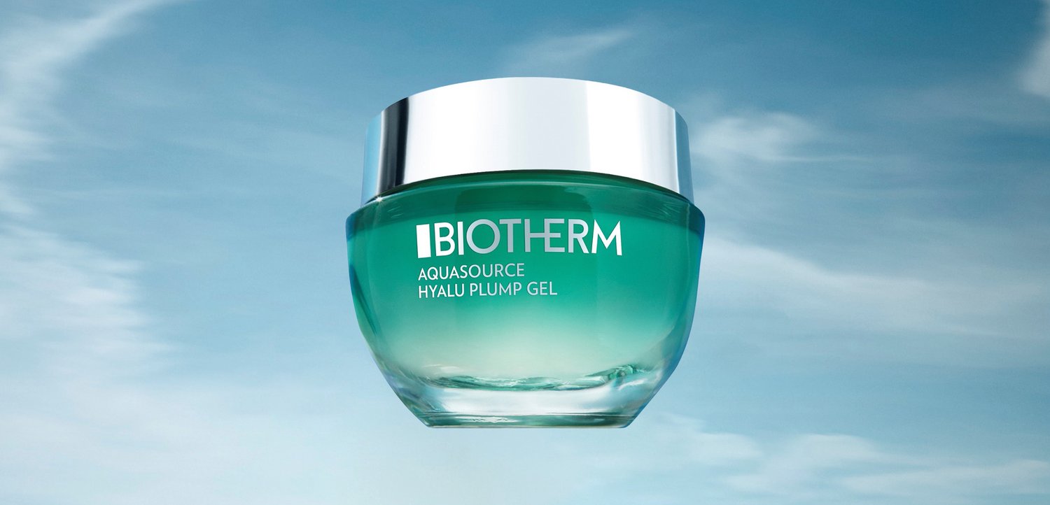 Aqua grøn gel crème i en klar krukke med et sølv låg, præsenteret mod en blød blå himmel baggrund. Teksten lyder "Biotherm Aquasource Hyalu Plump Gel."