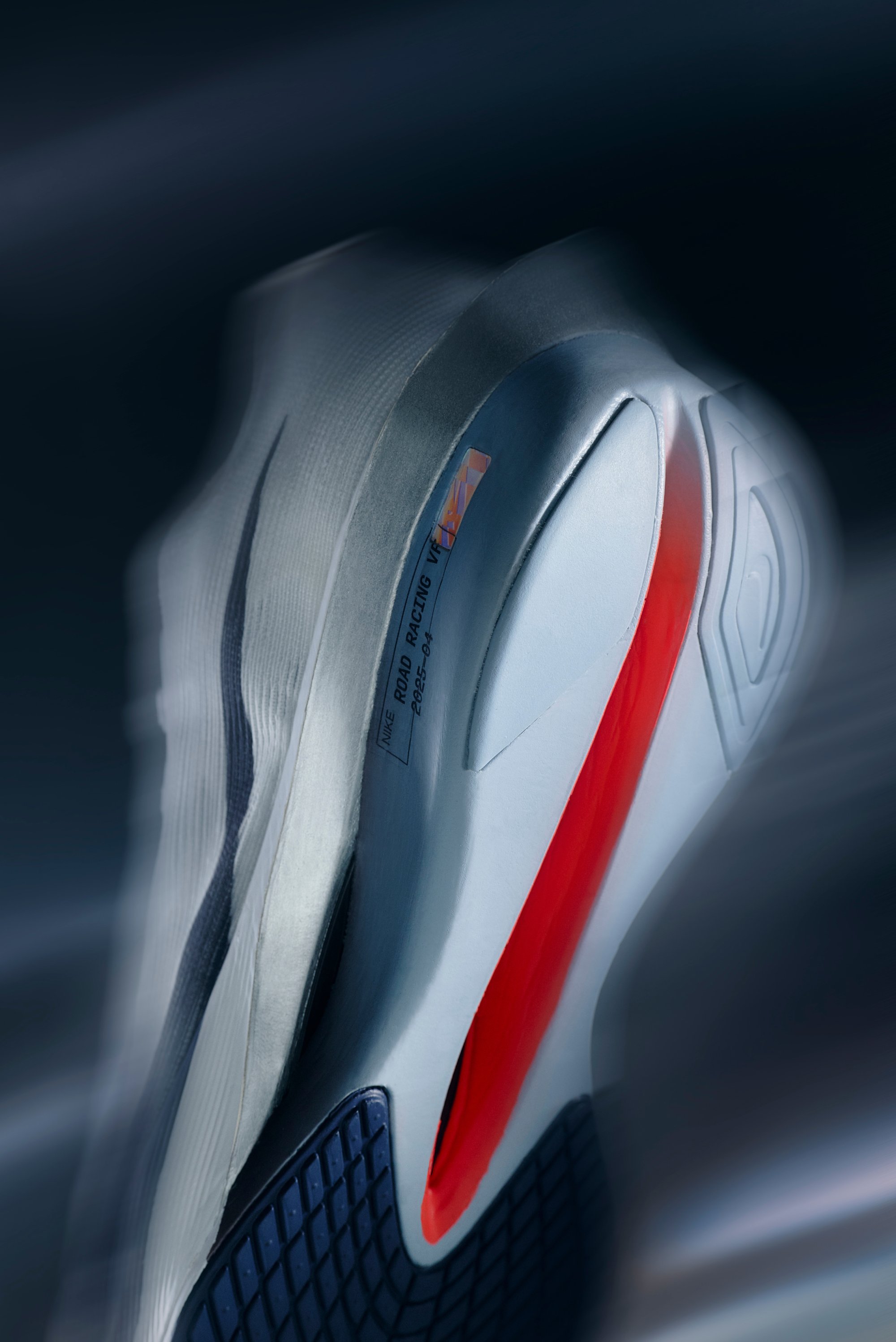 Nike hardloopschoen met een slank, wit bovenmateriaal, opvallende rode accenten en een gestructureerde zwarte zool met een geometrisch patroon.