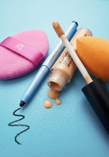 Éponge à maquillage rose, crayon eye-liner noir traçant un trait, anticernes liquide beige dégoulinant avec applicateur, et éponge de mélange orange sur une surface bleue.
