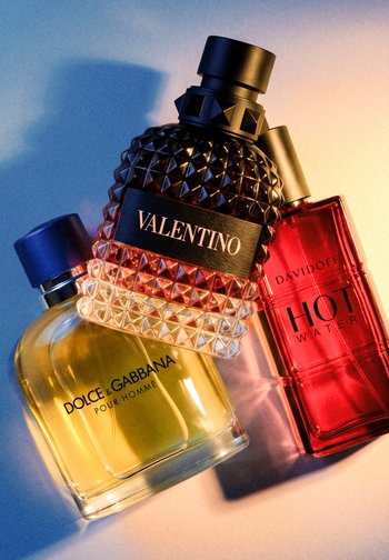 Three men's cologne bottles, Dolce & Gabbana Pour Homme in clear glass, Valentino with studded design, and red Davidoff Hot Water.