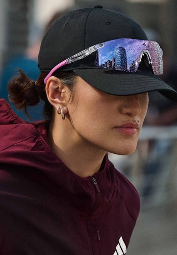Person wearing black cap with reflective sports sunglasses resting on the brim and a maroon jacket with a zipper.