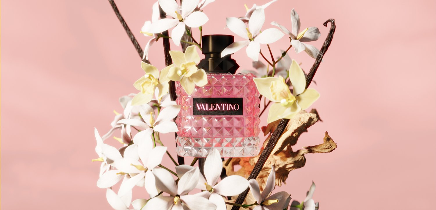 Valentino perfume bottle with a textured pink glass design surrounded by white and yellow flowers on a soft pink background.