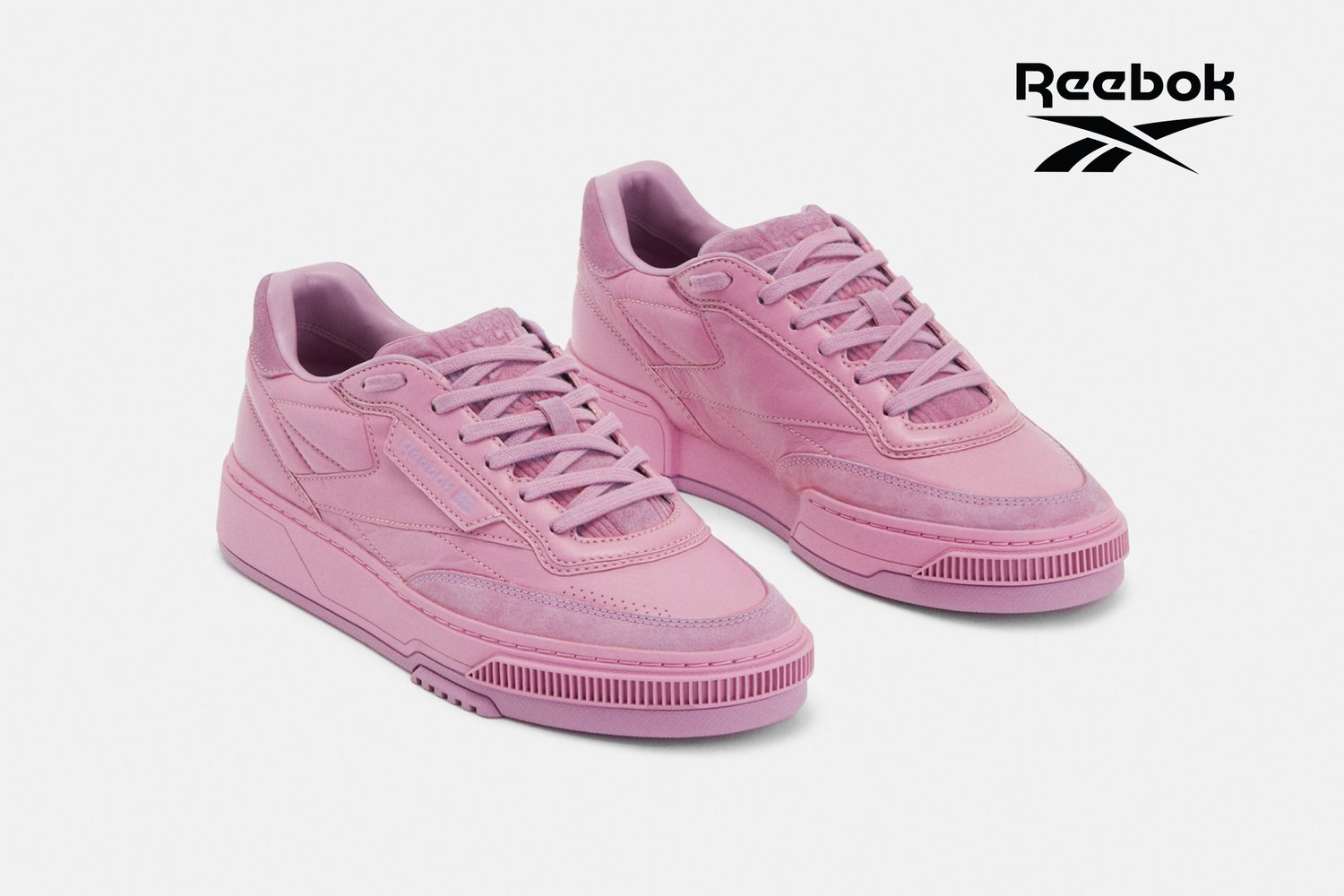 Zapatillas de deporte de cuero y gamuza rosa con costuras detalladas, punta redondeada y suela de goma texturizada. Logotipo de Reebok exhibido en la esquina.