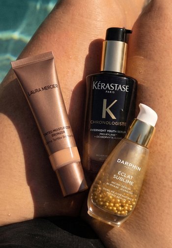 Trzy produkty do pielęgnacji skóry na opalonych nogach: tonujący nawilżający bronzer Laura Mercier, serum młodości na noc Kérastase oraz podwójne odmładzające mikro-serum Darphin.