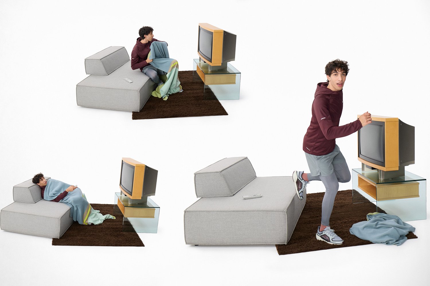 Young man in a maroon hoodie sitting and lying on a modern gray couch, with a colorful blanket, interacting with an old television.