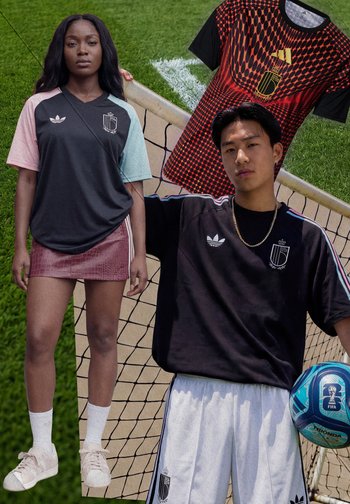 Deux modèles portant des maillots de sport noirs avec des accents blancs et roses, debout près d'un but de football avec un ballon bleu et un maillot rouge à motifs.