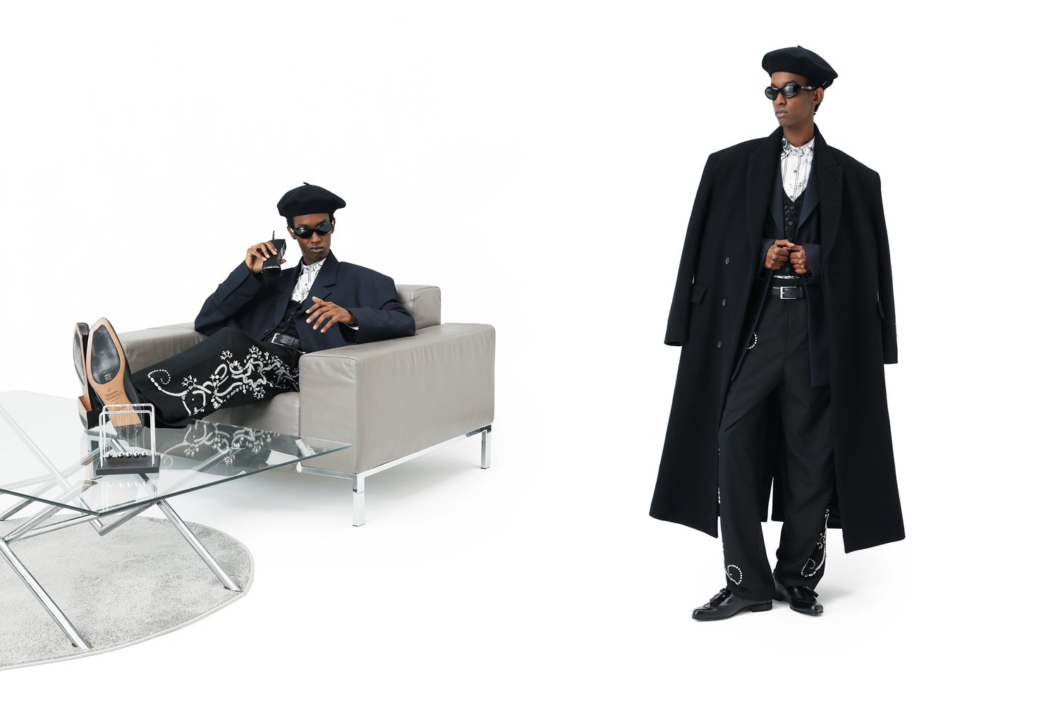 A fashionable individual relaxes on a grey sofa, sporting sunglasses and a beret, complemented by ornate black trousers and a long coat.