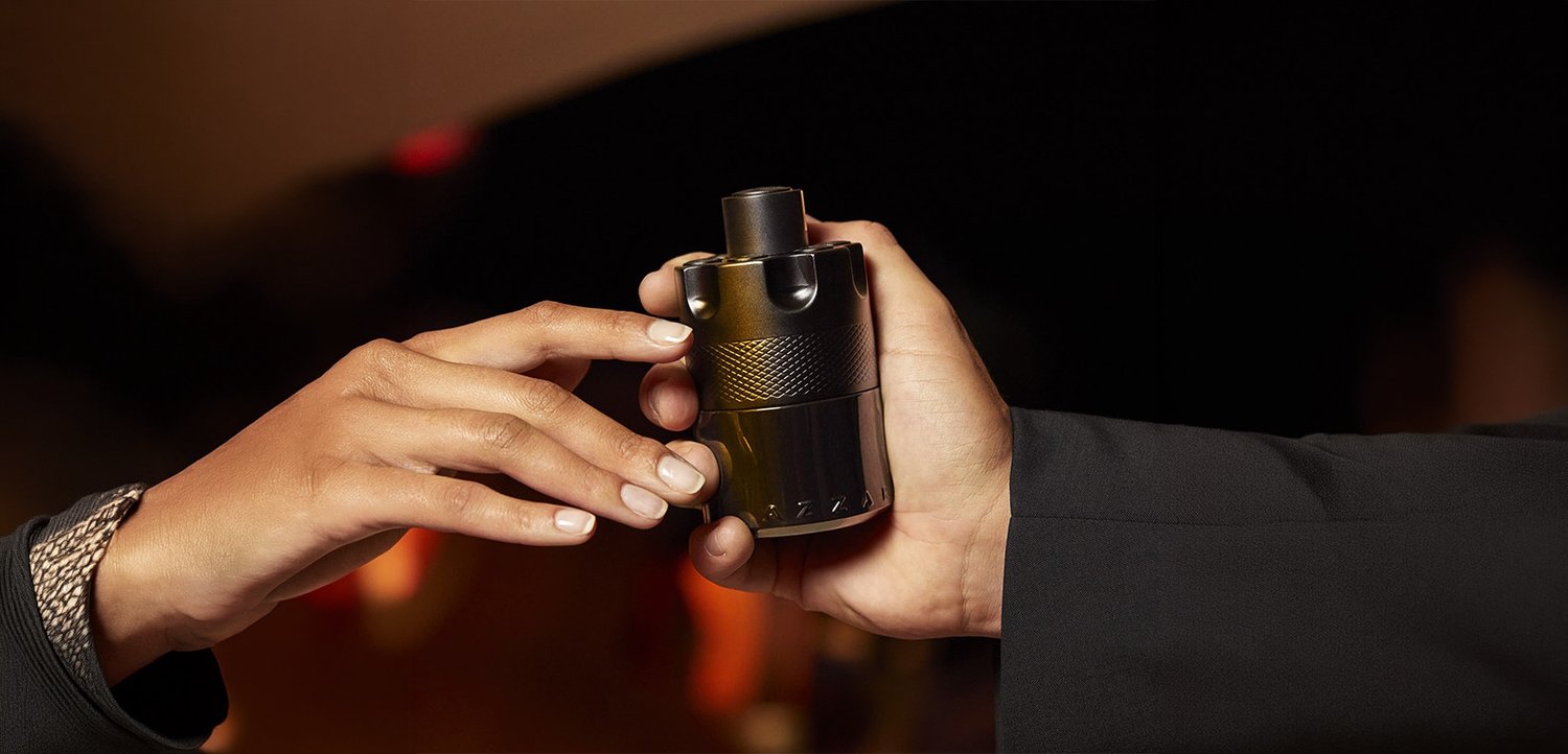 Deux mains échangent un objet cylindrique noir avec une prise texturée sur un fond sombre et flou.