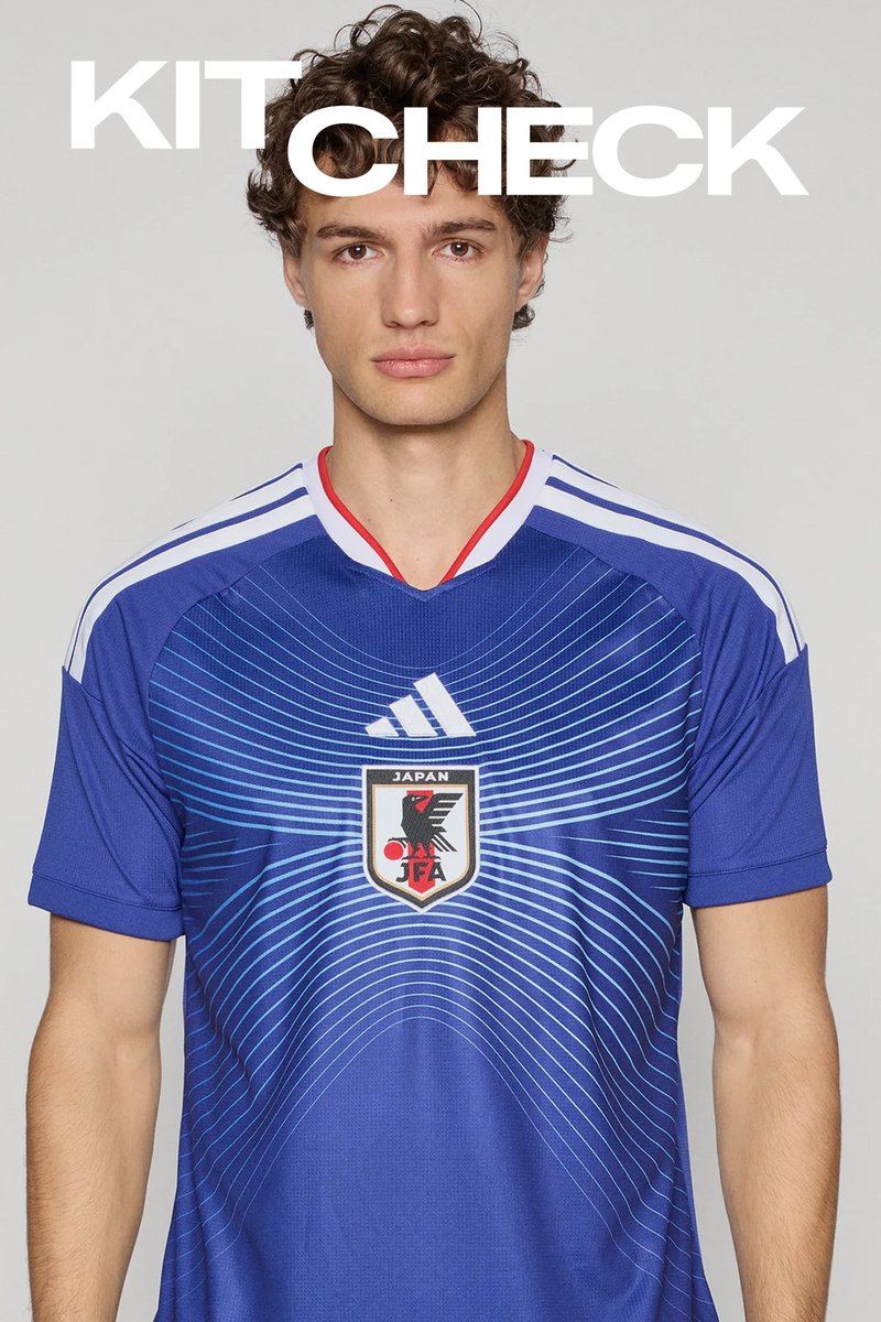 Młody mężczyzna w niebieskiej koszulce reprezentacji Japonii w piłce nożnej z białymi i czerwonymi wykończeniami, stojący na jasno szarym tle z tekstem "KIT CHECK" powyżej.