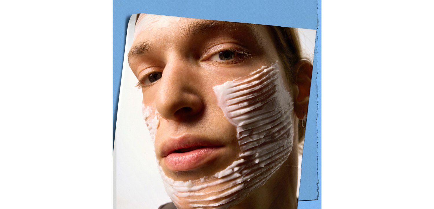 Nahaufnahme eines Gesichts mit aufgetragener weißer Creme, die in dicken, welligen Linien strukturiert ist. Helle Hauttönung, natürliche Lippen und ein neutraler Hintergrund.