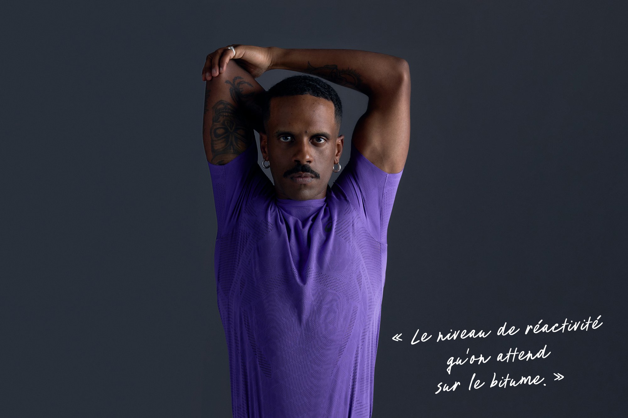 T-shirt de sport violet à manches courtes, avec un motif texturé. Le modèle pose avec les bras levés et se tient devant un fond sombre.