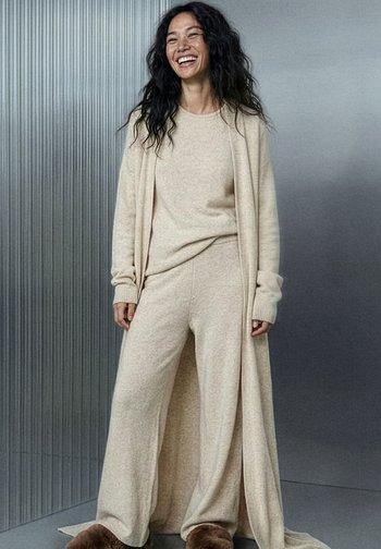 Beige gebreid loungewear-set bestaande uit een lange vest, een loszittend shirt en wijde broek, met een zachte textuur en geribde manchetten.