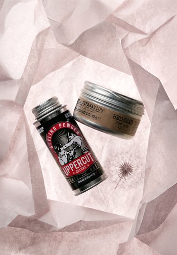 Productos para peinar el cabello sobre un papel arrugado de color rosa pálido, con una cabeza de semilla de diente de león debajo.