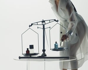 A person in a sheer white coat measures products on a scale, balancing a red bottle, a black box, and a blue spray on opposite sides.