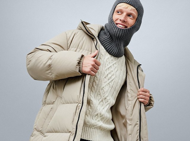 Beige puffjacka med dragkedja, stickad grå balaklava och krämfärgad kabelstickad tröja med ribbad textur och avslappnad passform.