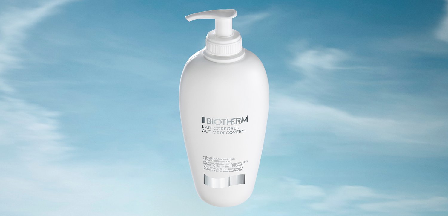 Hvid flaske med Biotherm Active Recovery body milk med pumpe top, mærket med produktinformationer, mod en blød blå himmel baggrund.