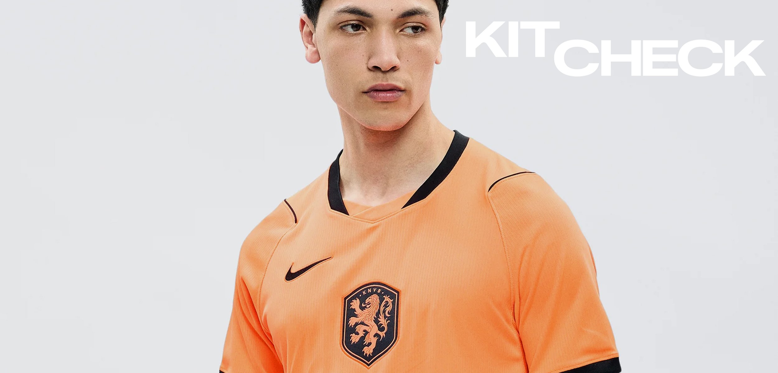 Junger Mann trägt ein oranges Sporttrikot mit einem schwarzen Löwenemblem und Nike-Logo, schaut leicht seitlich vor schlichtem Hintergrund.