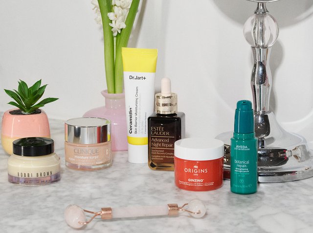Produits de soin de la peau comprenant la crème Bobbi Brown, Clinique Moisture Surge, la crème Dr. Jart+ Ceramidin, le sérum Estée Lauder, la crème Origins GinZing et le sérum Aveda sur une surface en marbre.