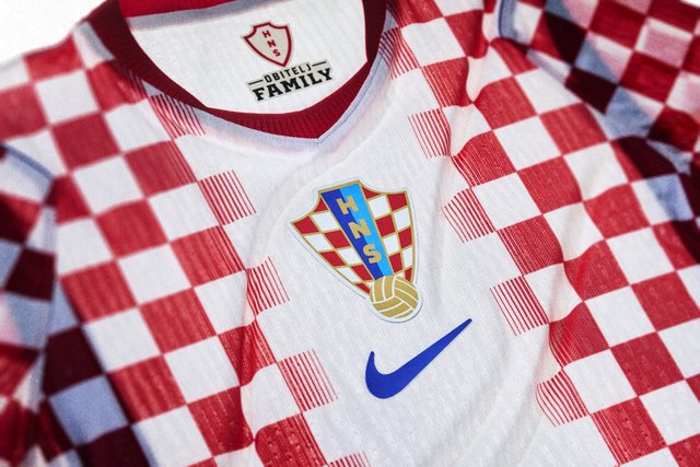 Chorwacka narodowa koszulka piłkarska z czerwono-białym wzorem w kratę, emblematem HNS, logo Nike oraz napisem „Obitelj Family” wewnątrz kołnierza.