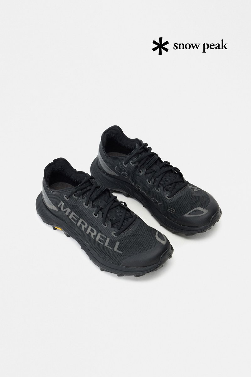Par af sorte Merrell trail løbesko med teksturerede såler og snørebånd, vinklet på en hvid baggrund med Snow Peak-logo over.