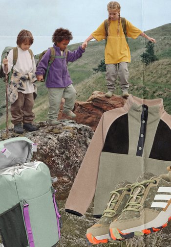 Τρία παιδιά πεζοπορούν σε εξωτερικό χώρο πάνω σε βράχια, κρατώντας τα χέρια τους· φαίνεται πεζοπορικό σακίδιο, μπεζ και μαύρο φλις μπουφάν και μπεζ παπούτσια για ορεινό τρέξιμο.