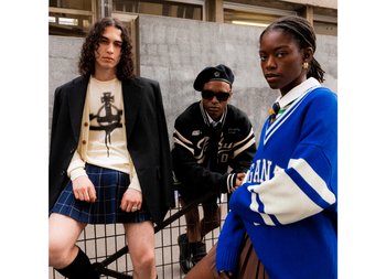 Drei junge Erwachsene posieren zusammen und präsentieren unterschiedliche Mode-Stile. Einer trägt ein schwarzes Blazer über einem Grafikhemd, ein anderer hat Sonnenbrillen und eine Collegejacke an, und der dritte trägt einen blauen Pullover mit Streifen.