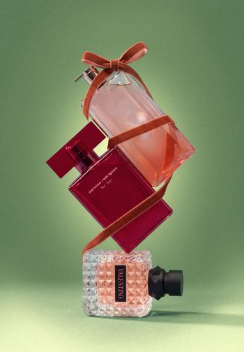 Trois flacons de parfum empilés et entourés d’un ruban couleur rouille sur fond vert. Les parfums sont de Narciso Rodriguez et Valentino.