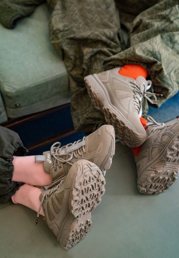 Twee paar wandelschoenen, één in lichtgrijs en de ander met een oranje detail, staan op een groene ondergrond met gedeeltelijk zichtbare benen.