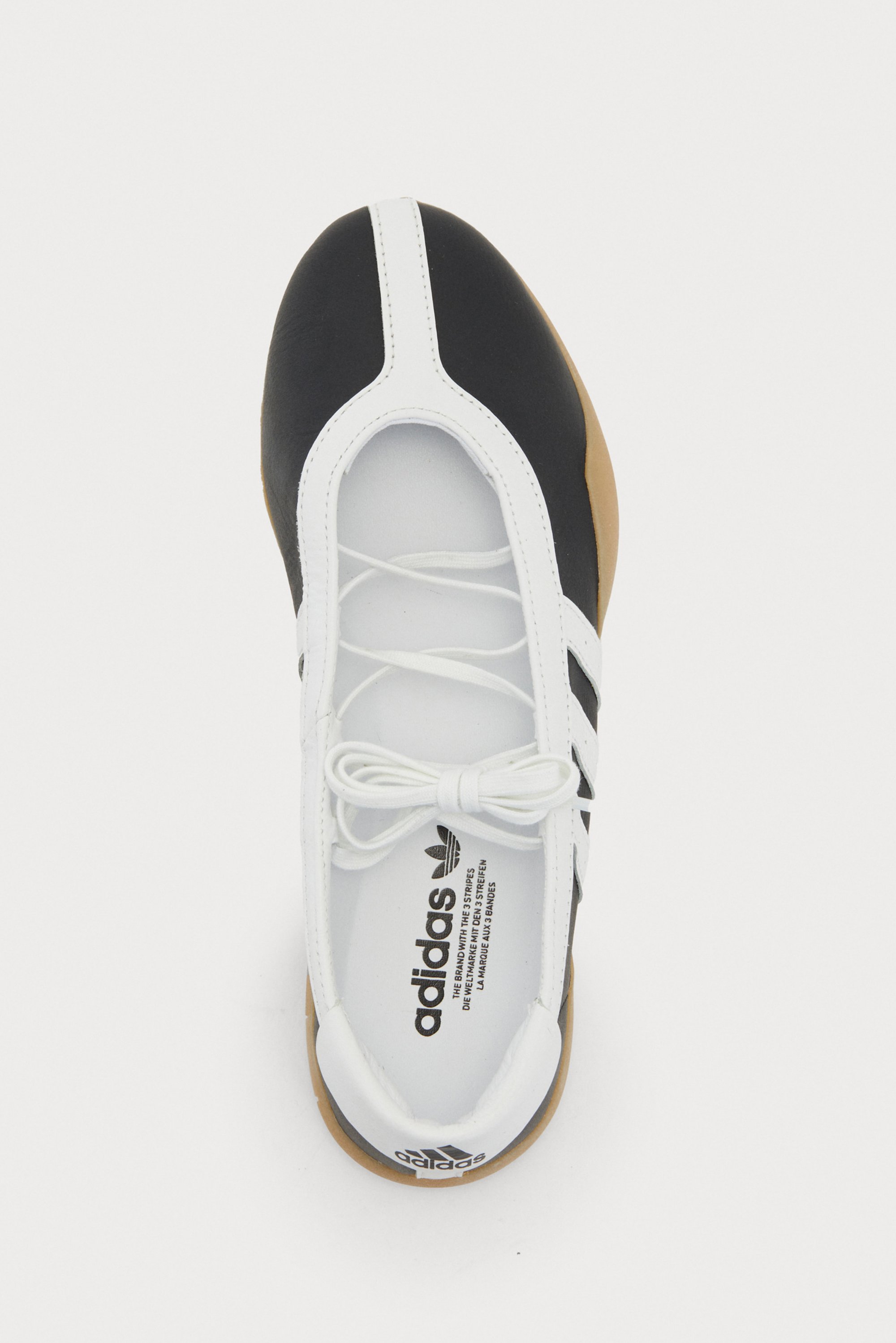 Black and white sports shoe with a rubber sole, featuring laces and a three stripes logo, shown from a top-down view.
