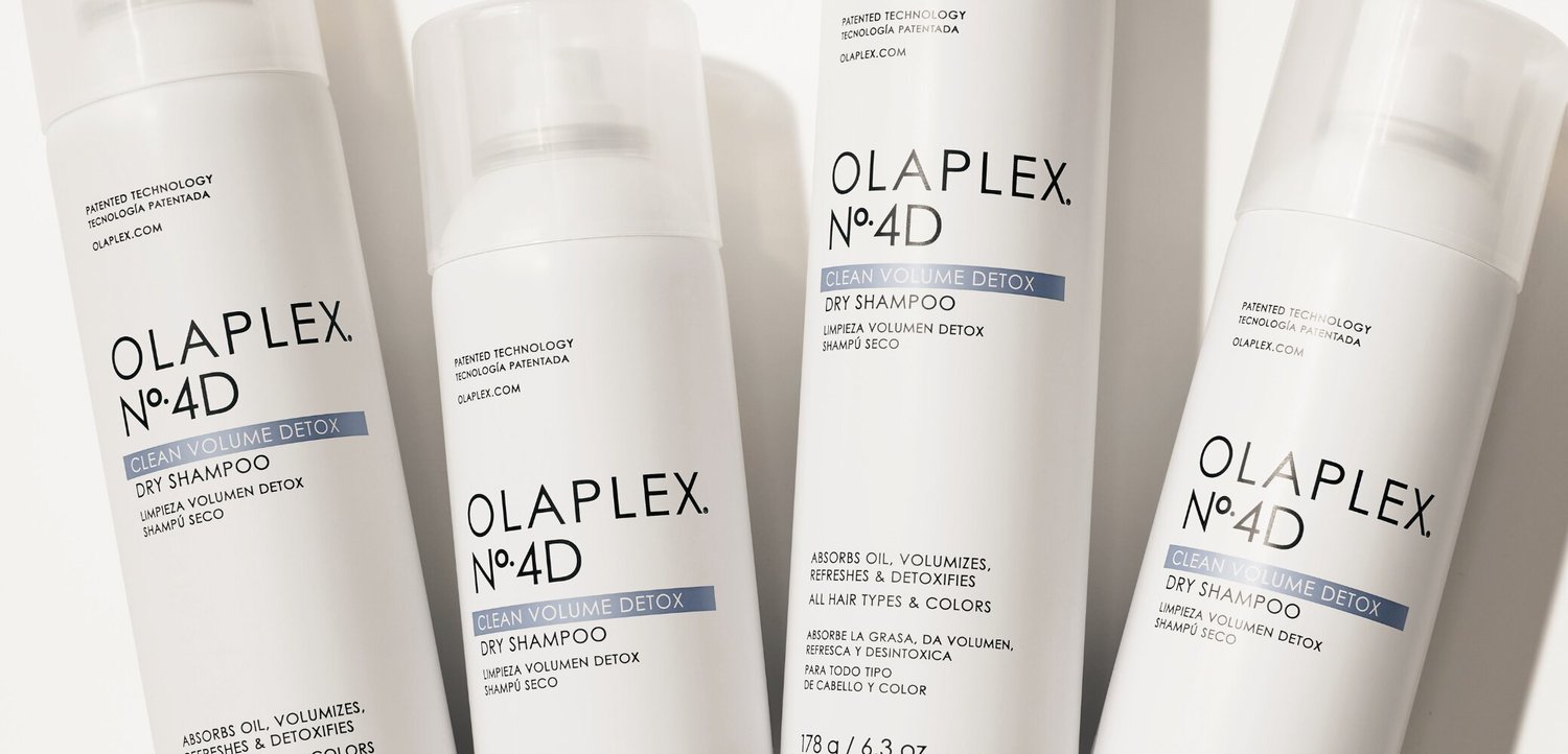 Cztery białe butelki suchego szamponu Olaplex No. 4D Clean Volume Detox ułożone blisko siebie na jasnej powierzchni.