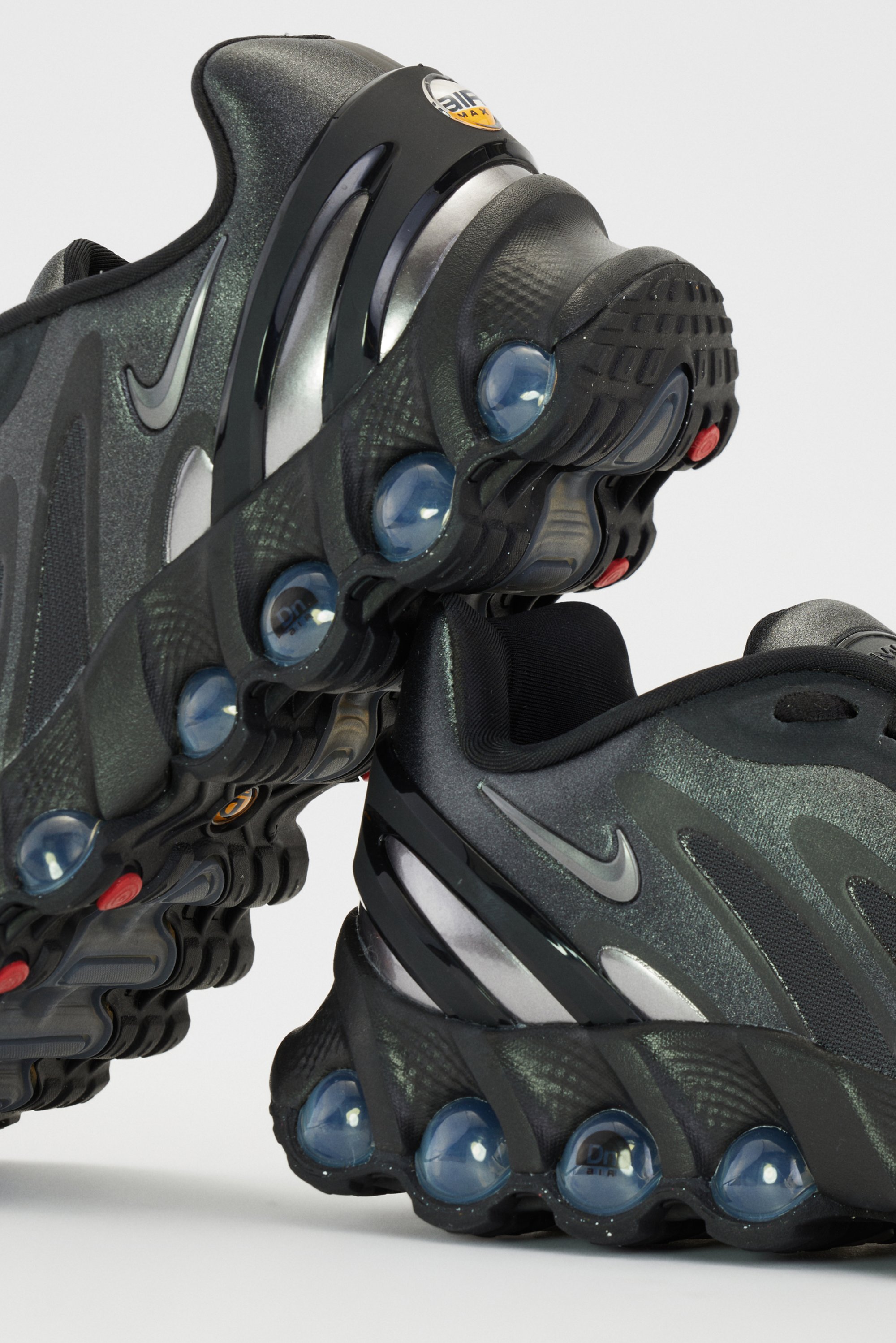 Zwarte Nike sneakers met glanzende accenten tonen een golvend ontwerp en transparante luchtkussens in de zool, tegen een effen achtergrond.