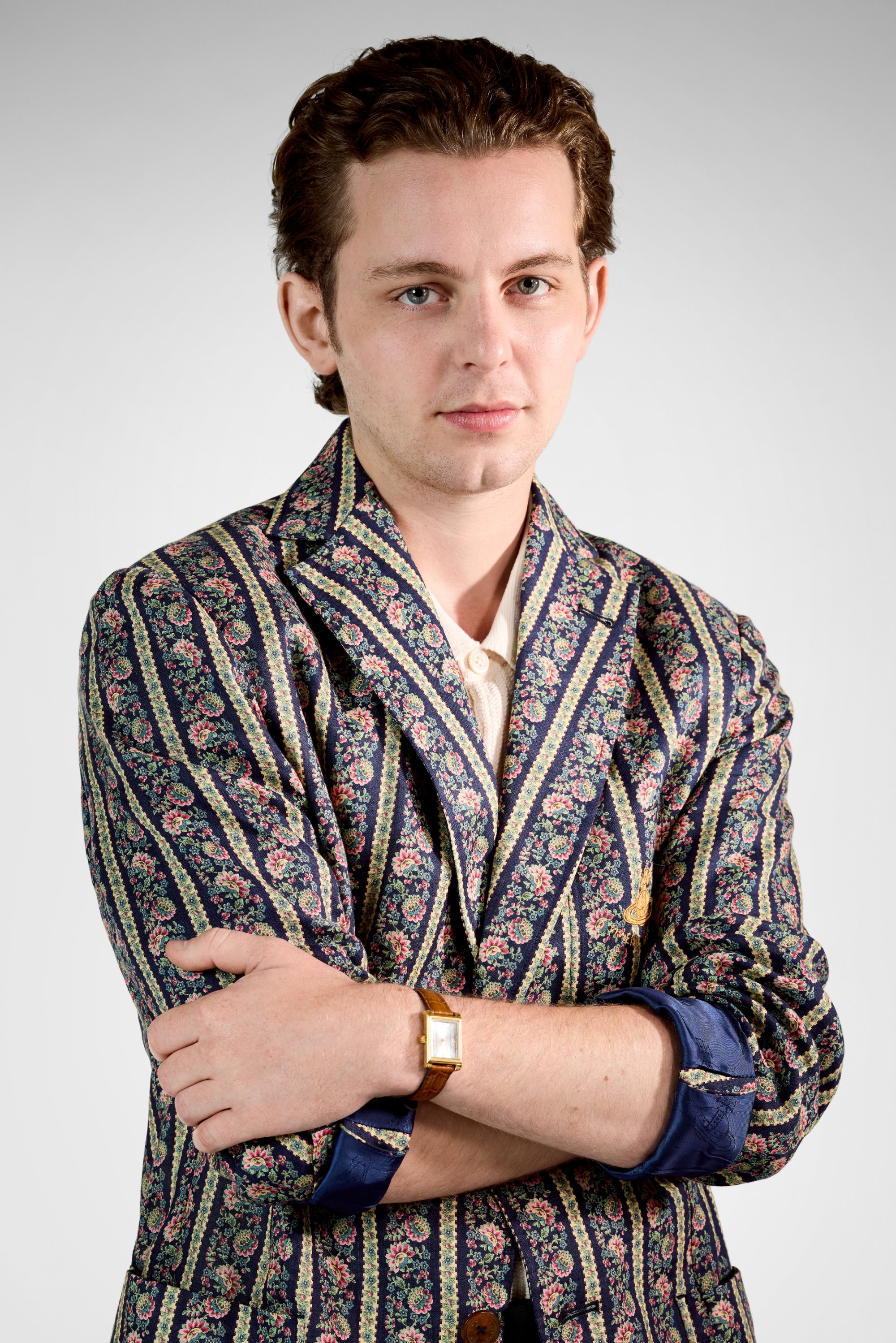 Blazer con estampado floral en rayas azul marino y crema, que presenta un cuello chal y mangas remangadas. Se puede ver un reloj dorado con una correa de cuero marrón.