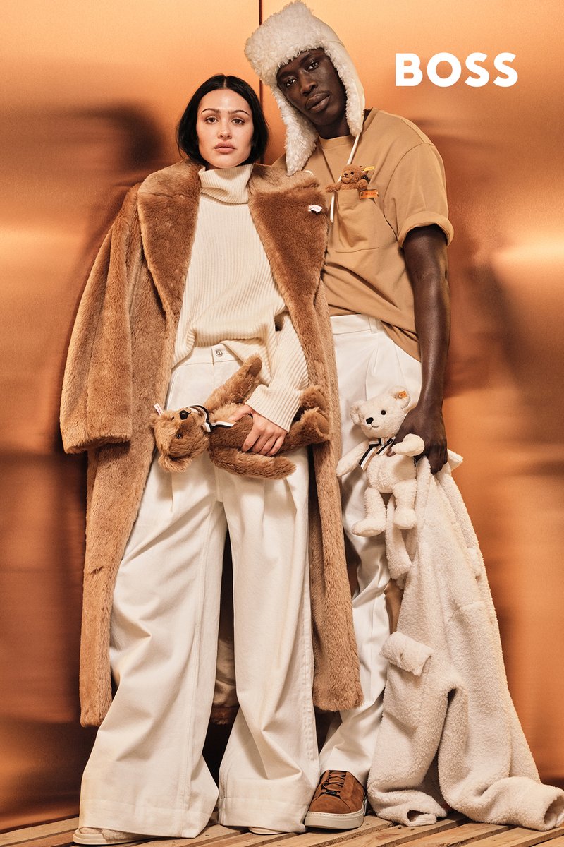 Twee modellen staan tegen een gouden achtergrond. De ene draagt een bruine nepbonten jas en een crème coltrui; de andere draagt een beige overhemd met een zakje en een bontmuts.