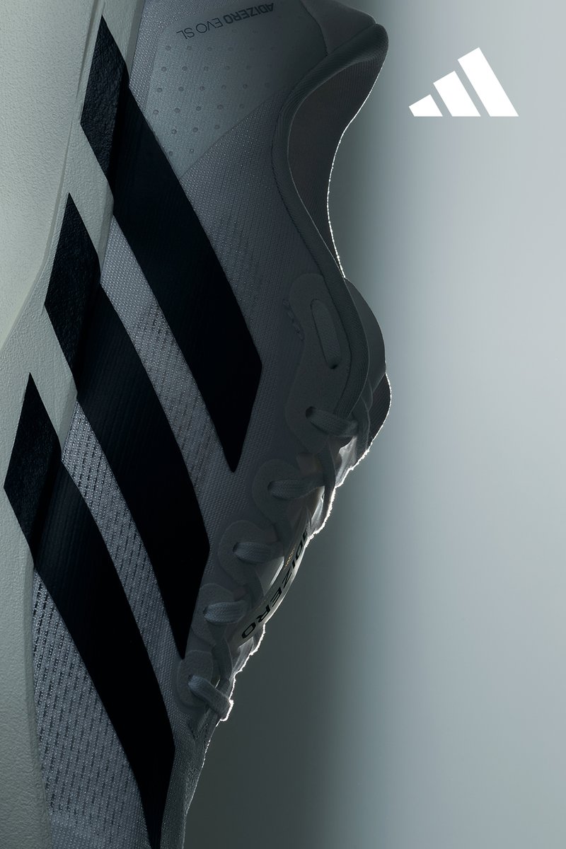 Una zapatilla de running blanca con rayas negras, situada sobre un suave fondo gris, que resalta su diseño elegante y la marca.