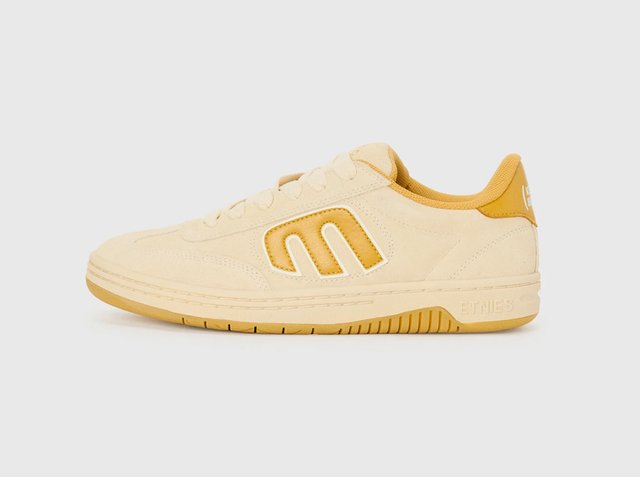 Low-top beige and mustard yellow sneaker with lace-up front and stylized "E" logo on the side, flat rubber sole, and padded collar.