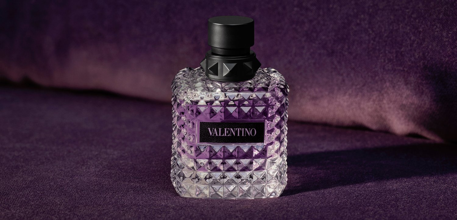 Vierkante glazen parfumfles met een zwarte dop en Valentino-label op een paarse fluwelen ondergrond.