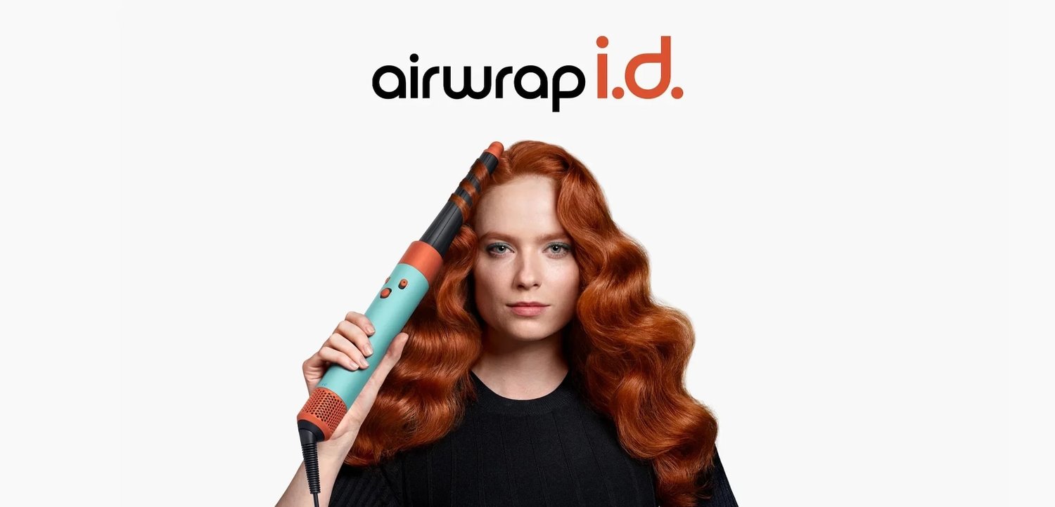 Kvinde med langt rødt hår, der bruger et teal- og orange Airwrap hårstylingværktøj, med "airwrap i.d." tekst ovenfor på en hvid baggrund.