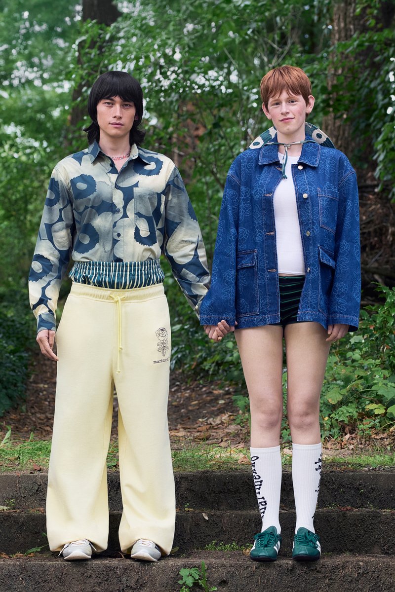 Zwei Personen halten Händchen, einer trägt ein gemustertes Hemd und helle, weite Hosen, der andere eine blaue Jacke und Shorts mit gestreiften Socken.