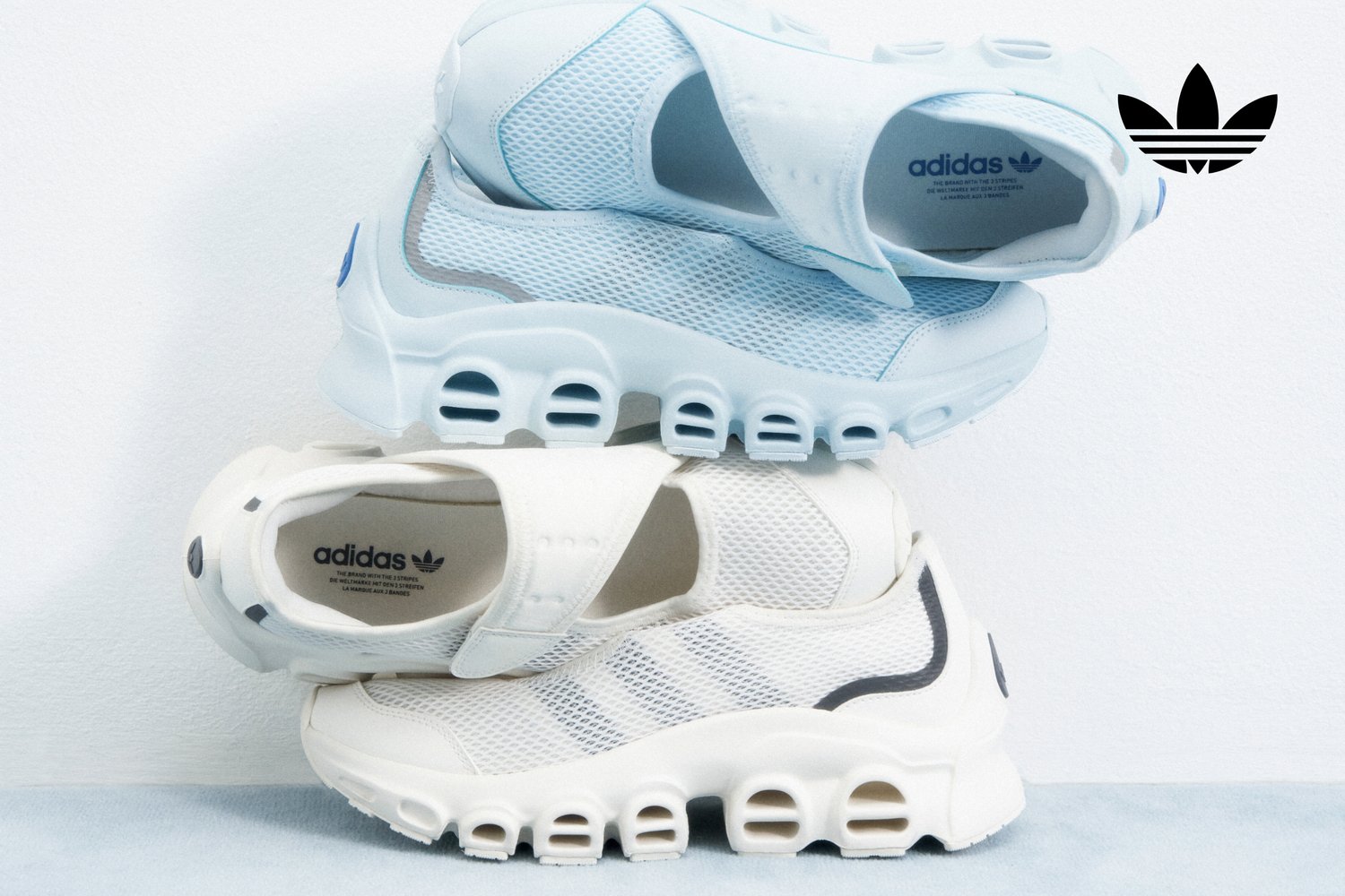 Tres pares de zapatillas Adidas apilados, con diseños en azul claro y blanco, fabricados con tejido de malla y patrones de agujeros distintivos.