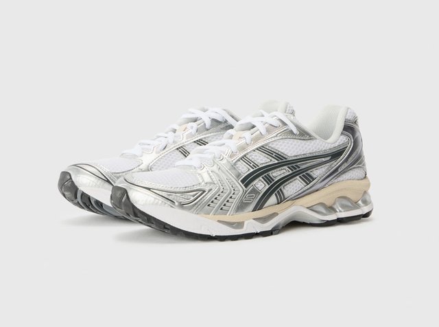 Paire de chaussures de course blanches et argentées avec des accents noirs, des lacets blancs et une semelle amortissante sur un fond gris clair uni.
