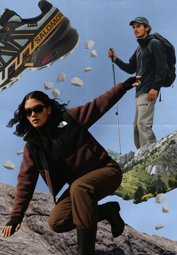 Juodos ir rudos spalvos vilnonis švarkas, pilkos spalvos lauko kelnės, pilki žygio batai su geltonomis detalėmis, saulės akiniai ir kuprinė su žygių lazdomis.