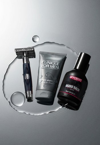 Rasoir avec un manche bleu, tube de crème à raser grise et bouteille de baume à barbe noire sur une surface mouillée avec des gouttes d'eau.