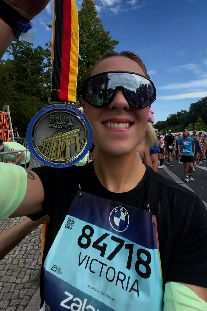 Silbermedaille hängt an einem dreifarbigen Band, zeigt das Design des Brandenburger Tors. Teilnehmer trägt ein schwarzes Shirt und übergroße Sonnenbrille.