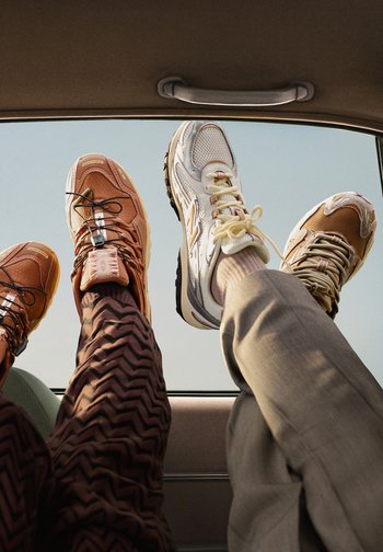 Två par sneakers i bilen: ett par i tan nät med detaljer, det andra i vitt nät med beige och svarta accenter. Texturerade byxor synliga.
