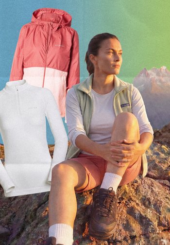 Frau sitzt bei Sonnenuntergang auf felsigem Berggelände, trägt Wanderschuhe und Weste, neben ihr sind zwei Outdoor-Jacken zu sehen.
