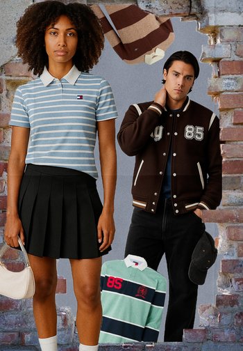 Gestreiftes blaues Polo mit Kragen, schwarze Faltenrock; braune Varsity-Jacke mit weißen Akzenten, Modell trägt dunkle Jeans und eine Kappe.