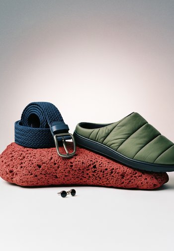 Roheline polsterdatud libisev king, tumesinine kangast vöö hõbedase pandlaga ja mustad ümmargused mansetinööbid poorse punase kivi peal heledal taustal.