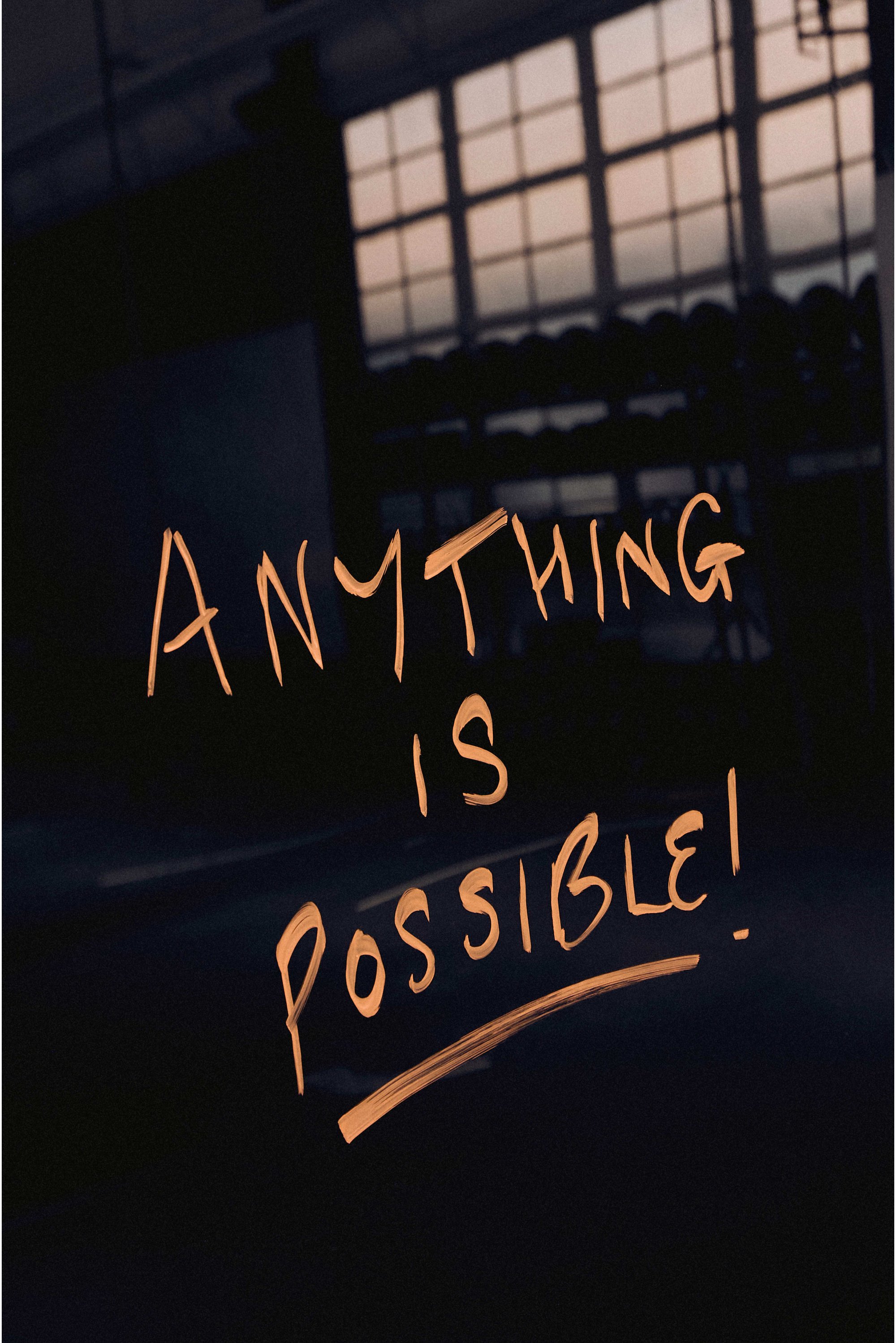 Na tmavom povrchu je napísané "VŠETKO JE MOŽNÉ!" v žiarivej oranžovej farbe, s rozmazaným pozadím telocvične viditeľným cez okno.