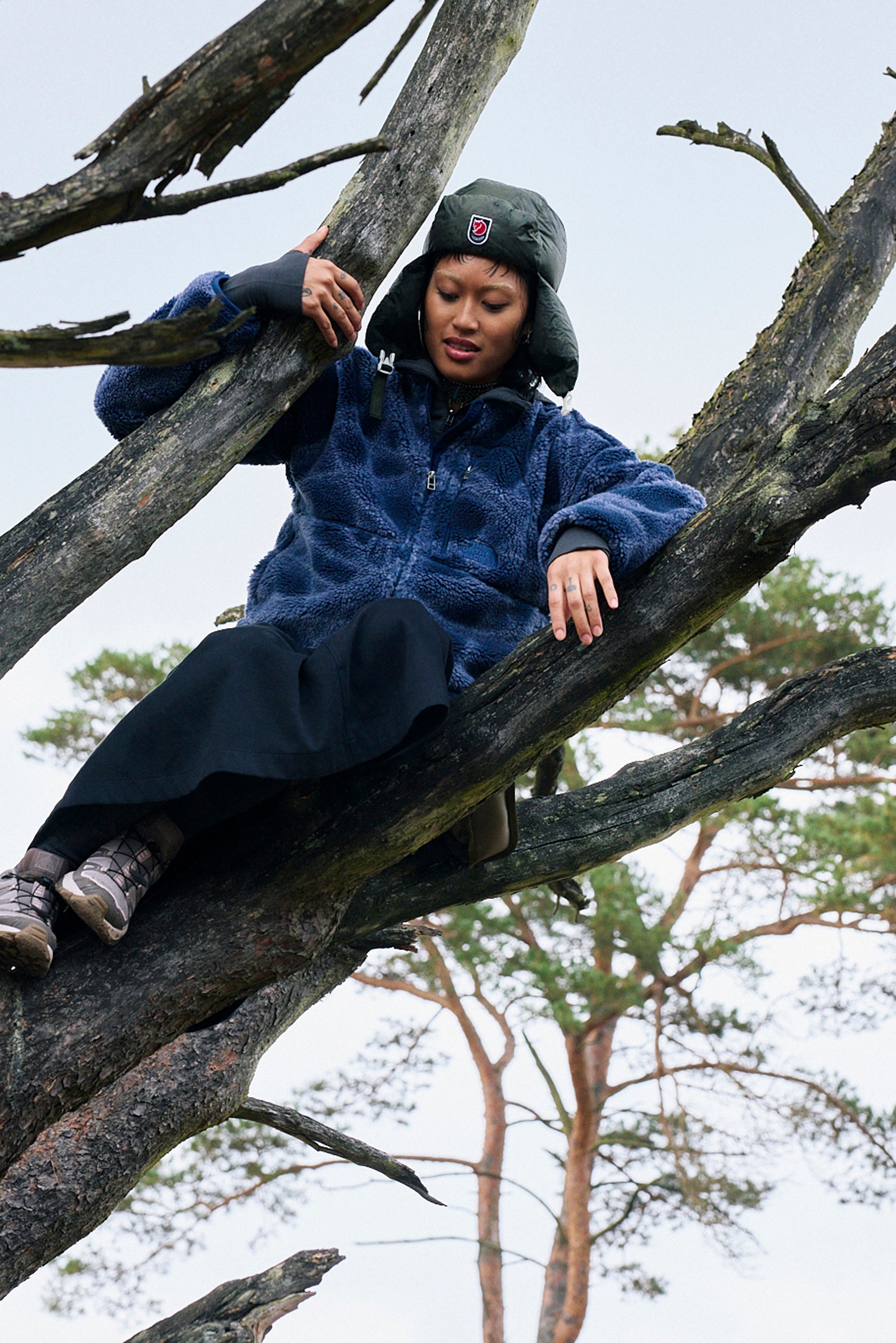 Navy fleece jacket with a patterned texture, teamed with a long black skirt and grey hiking boots, sitting on a tree branch.